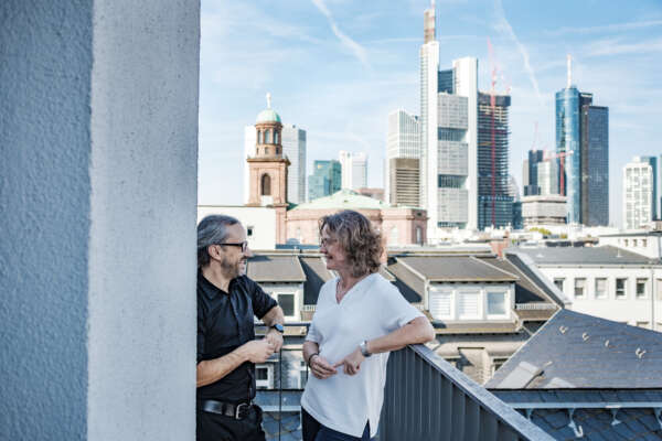 Monica Wellmann und Markus Fertig auf dem Balkon des Haus des Buches in Frankurt am Main. Sie unterhalten sich vor Frankfurter Kulisse.