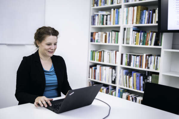 Daniela Kahl sitzt an einem Laptop in einem Büro vor einer Bücherwand.